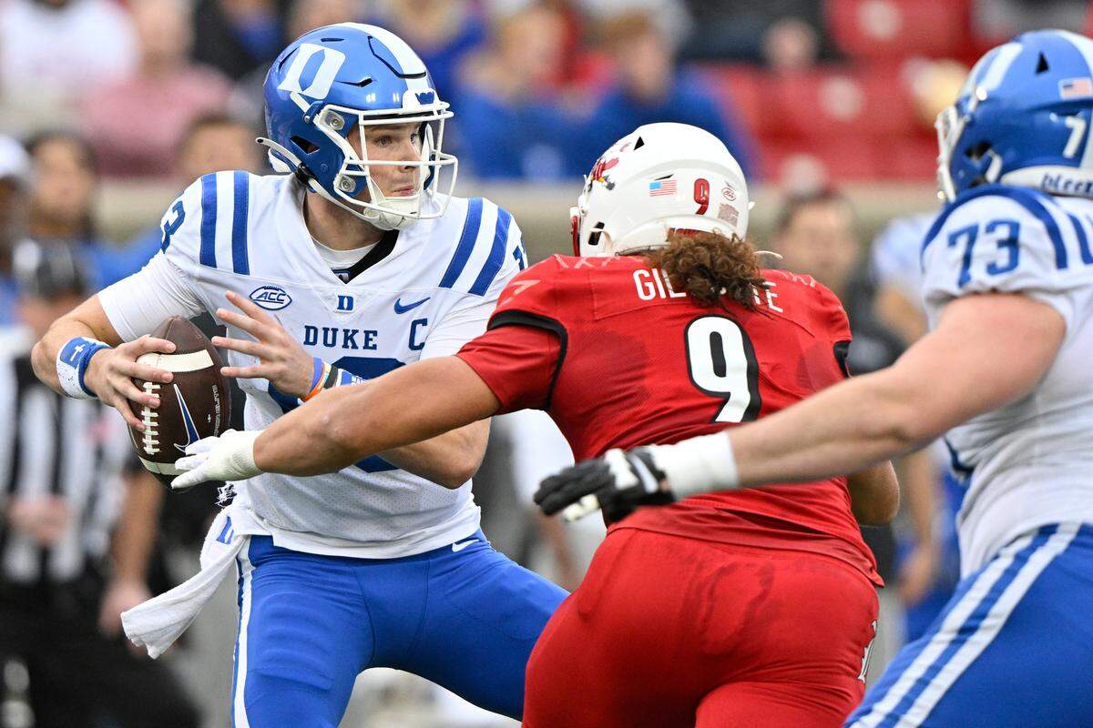 Duke Blue Devils quarterback Riley Leonard (13) tries to avoid a sack by Louisville Cardinals defensive lineman Ashton Gillotte (9) during the second quarter at L&N Federal Credit Union Stadium.