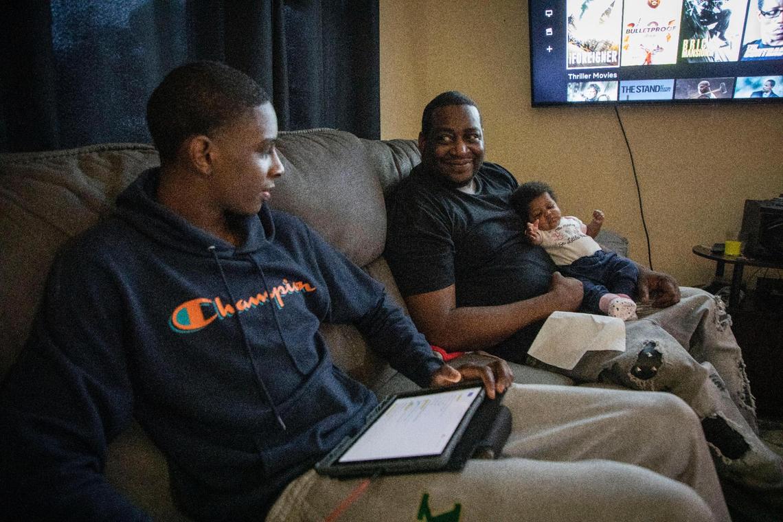Jyrah Canady does homework while sitting with his father Adrian and two-month-old baby sister Zarihanna at their home in Kinston, N.C. on Feb. 2, 2022.