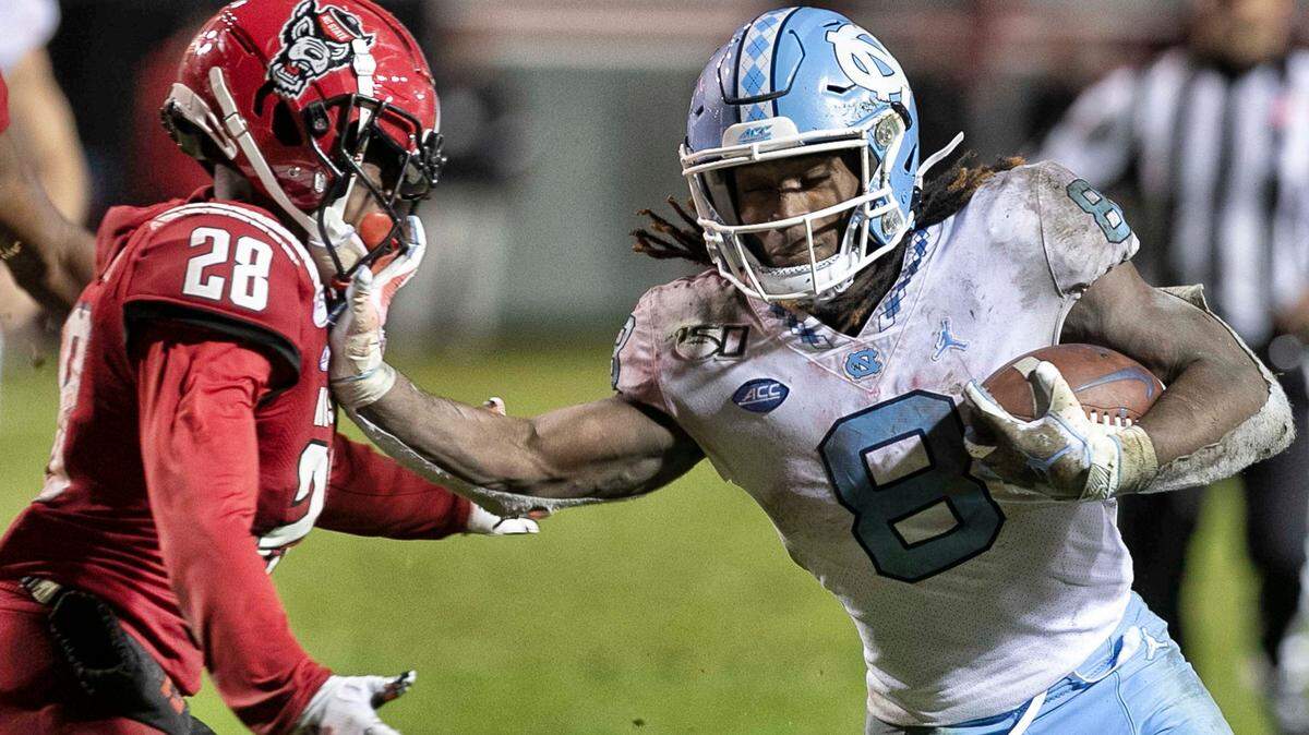 North Carolina’s Michael Carter (8) stiff-arms N.C. State’s Kishawn Miller (28) on a 38-yard gain in the fourth quarter on Saturday, November 30, 2019 at Carter-Finley Stadium in Raleigh, N.C.