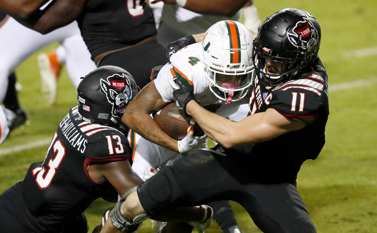 N.C. State linebacker Payton Wilson (11) and defensive back Tyler Baker-Williams (13) tackle Miami running back Jaylan Knighton (4) during the second half of Miami’s 44-41 victory over N.C. State at Carter-Finley Stadium in Raleigh, N.C., Friday, Nov. 6, 2020.