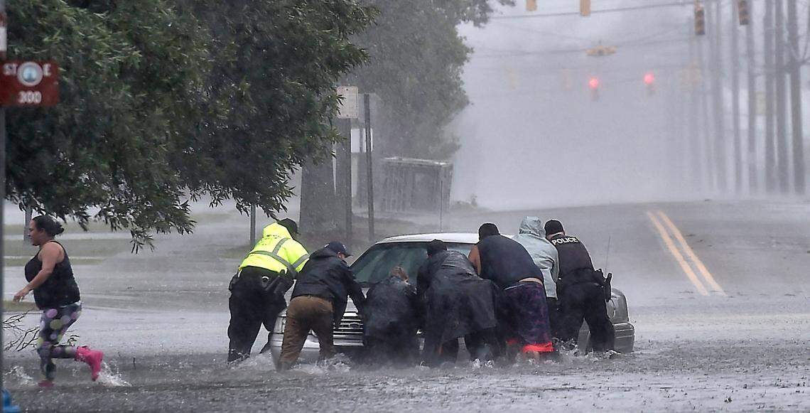 As torrential rain falls Saturday afternoon, Sept. 15, 2018 police officers help civilians push a stranded motorist out of the flood water near downtown Lumberton, NC.