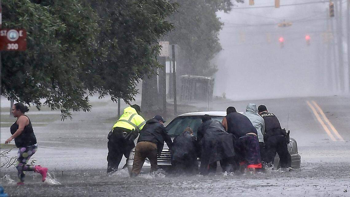 As torrential rain falls Saturday afternoon, Sept. 15, 2018 police officers help civilians push a stranded motorist out of the flood water near downtown Lumberton, NC.
