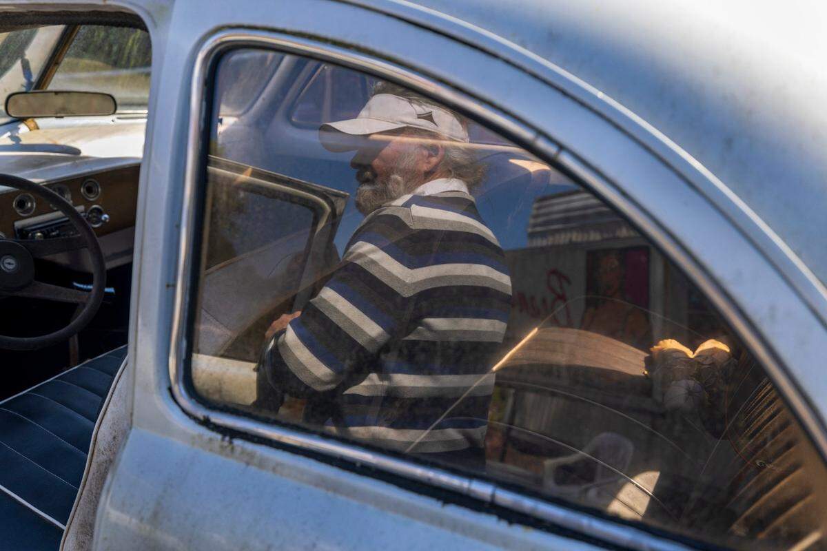 “Crazy Dale” Varnam is reflected in the window of one of this vintage Volkswagens on Thursday, February 22, 2024 in Varnamtown, N.C. Varnam has collected all types of vehicles, which are housed on 20 acres of his property.