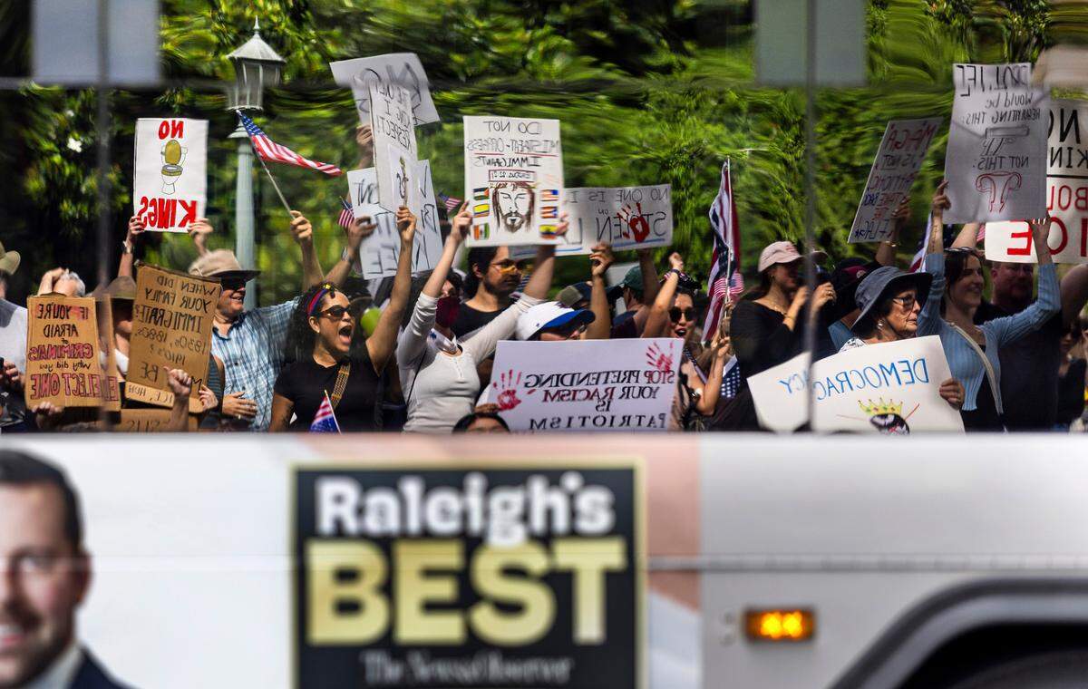 Demonstrators on the State Capitol grounds are reflected in the windows of a Raleigh Capital Area Transit bus as it passes them on S. Salisbury Street during the ‘No Kings’ rally on Saturday, June 14, 2025 in Raleigh, N.C.