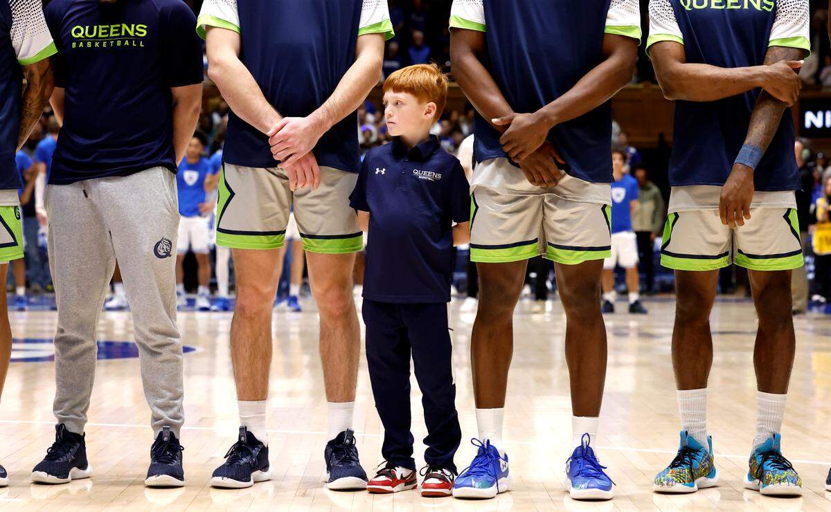 Queens associate head coach Charlie Wilson’s son, Logan, stands with the team during the national anthem before the Royals game against Duke at Cameron Indoor Stadium in Durham, N.C., Saturday, Dec. 30, 2023.