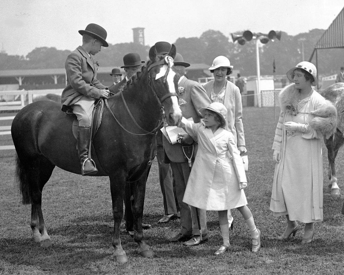 Britain’s Princess Elizabeth, later Queen Elizabeth II, pats a prize-winner’s horse from the children’s jumping class at the Richmond Royal Horse Show, June 15, 1934. The Duchess of York watches far right.