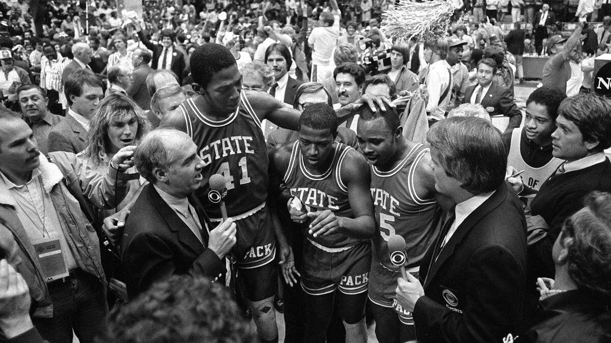 CBS announcer Billy Packer, left, interviews N.C. State seniors Thurl Bailey, Dereck Whittenburg, and Sidney Lowe after the Wolfpack won the National Championship on April 4, 1983. The Wolfpack won the game 54-52.