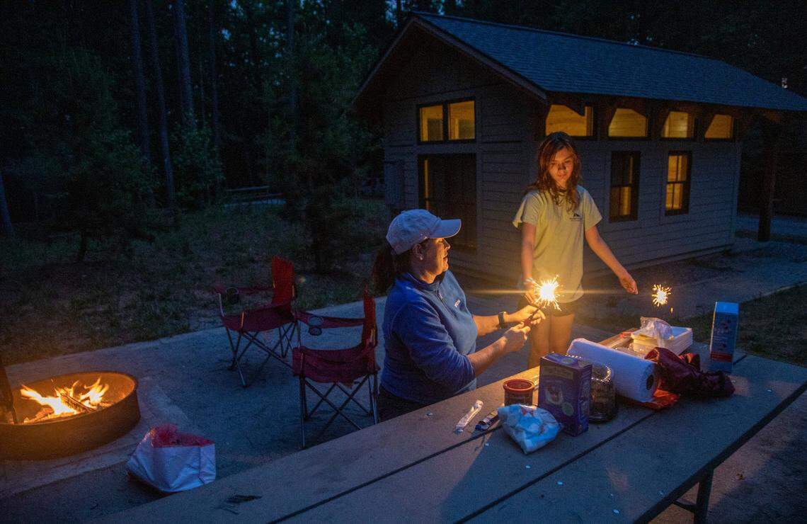 Victoria Taylor and her daughter Emma Grace, 12, light sparklers at one of the cabin rental sites in the family campground at Lake Norman State Park in Troutman.