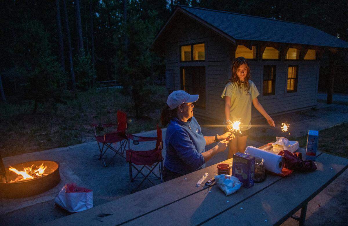 Victoria Taylor and her daughter Emma Grace, 12, light sparklers at one of the cabin rental sites in the family campground at Lake Norman State Park in Troutman. Cabin rental prices will stay the same, but N.C. State Parks will increase the prices for campsites starting May 1, 2025.