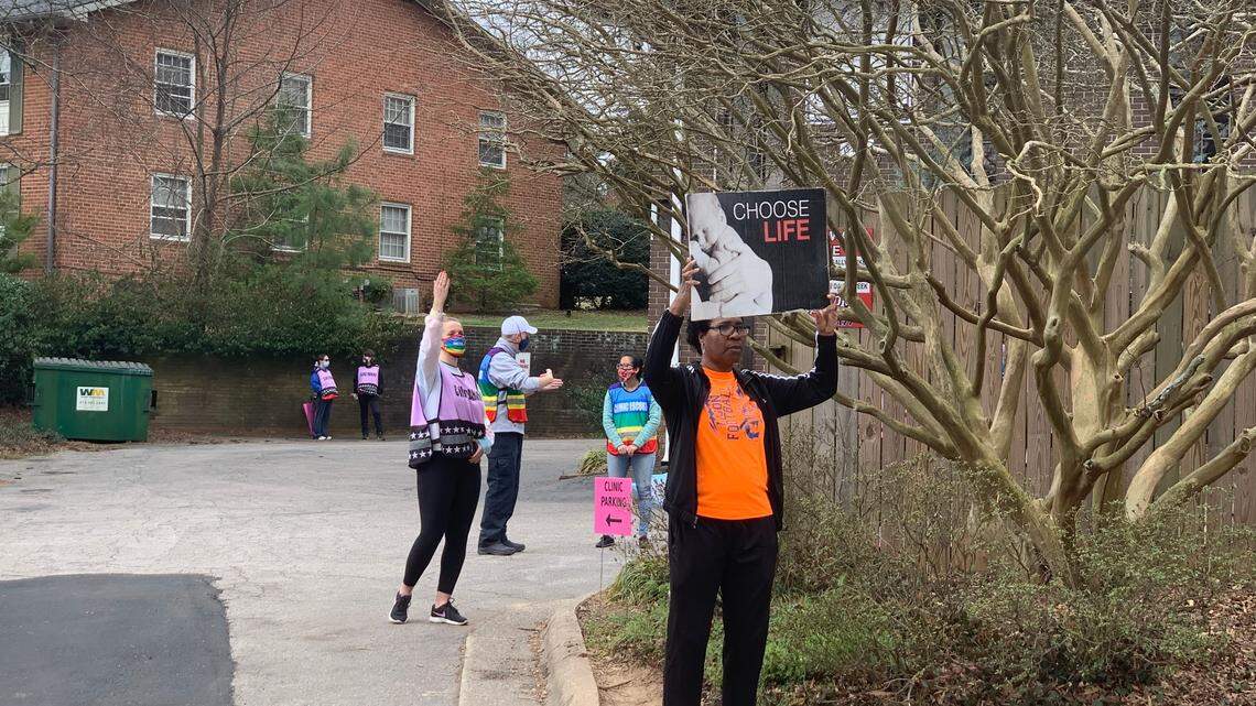 In this file photo, a volunteer at a Raleigh women’s clinic waves a woman into the parking lot, while a woman holds a “Choose Life” sign. Other escorts are on hand in the parking lot to help women make their way into the clinic.