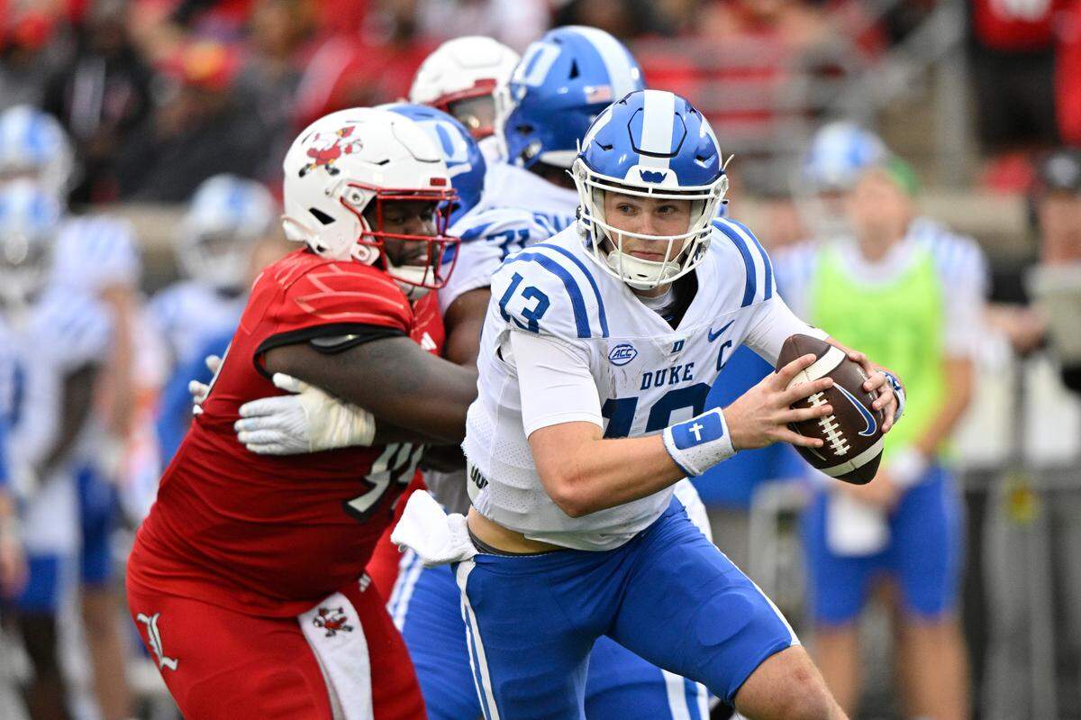 Duke Blue Devils quarterback Riley Leonard (13) scrambles away from Louisville Cardinals defensive lineman Dezmond Tell (99) during the second quarter at L&N Federal Credit Union Stadium.