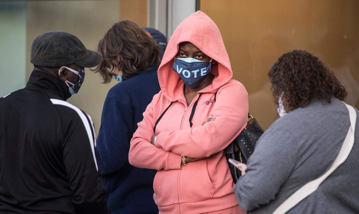 Maureen Olumhense waits outside the Durham County Main Library in Durham, N.C. to cast her vote on Thursday morning, Oct. 15, 2020, the first day of early voting.