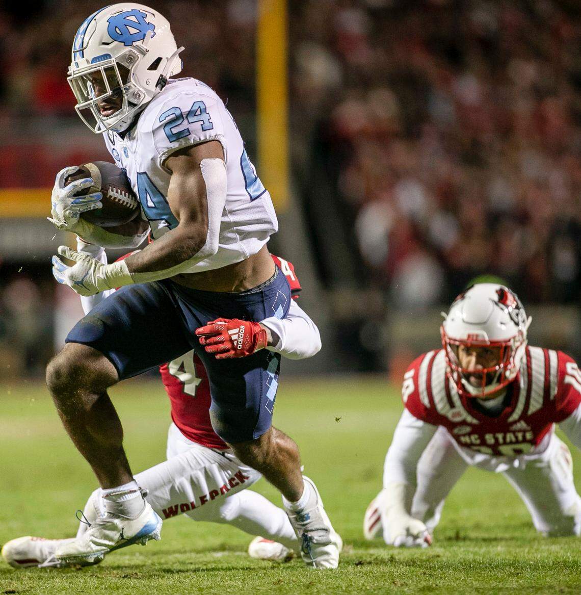 North Carolina’s British Brooks (24) breaks open for a 40-yard run in the first quarter as N.C. State’s Joshua Pierre-Louis (4) works to make the stop on Friday, November 26, 2021 at Carter-Finley Stadium in Raleigh, N.C.