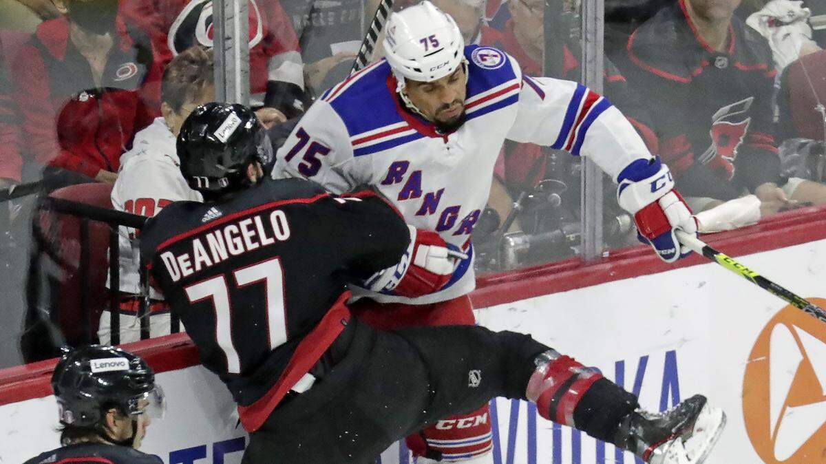 Carolina Hurricanes defenseman Tony DeAngelo (77) checks New York Rangers right wing Ryan Reaves (75) into the boards during the third period in Game 2 of an NHL hockey Stanley Cup second-round playoff series Friday, May 20, 2022, in Raleigh, N.C. (AP Photo/Chris Seward)