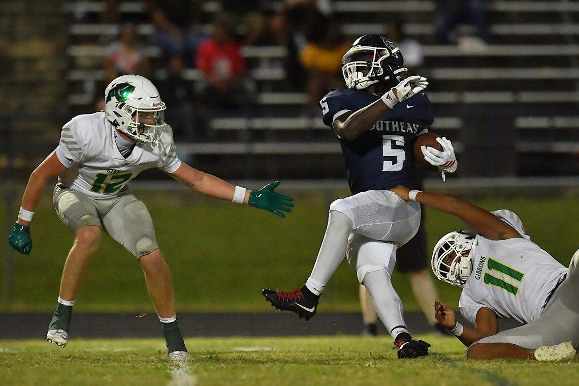 Southeast Raleigh running back Christian Freeman (5) runs for the first down against Cardinal Gibbons's Skylar Alston (11) and Drake Stone (12) during the second half. The Southeast Raleigh Bulldogs and the Cardinal Gibbons Crusaders met in a non-conference football game in Raleigh, N.C. September 12, 2025