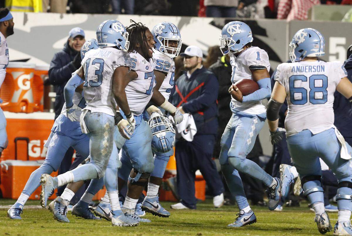 North Carolina offensive lineman Joshua Ezeudu (75) celebrates with defensive back Myles Dorn (1) after Dorn intercepted a pass during the second half of UNC’s 41-10 victory over N.C. State at Carter-Finley Stadium in Raleigh, N.C., Saturday, November 30, 2019.