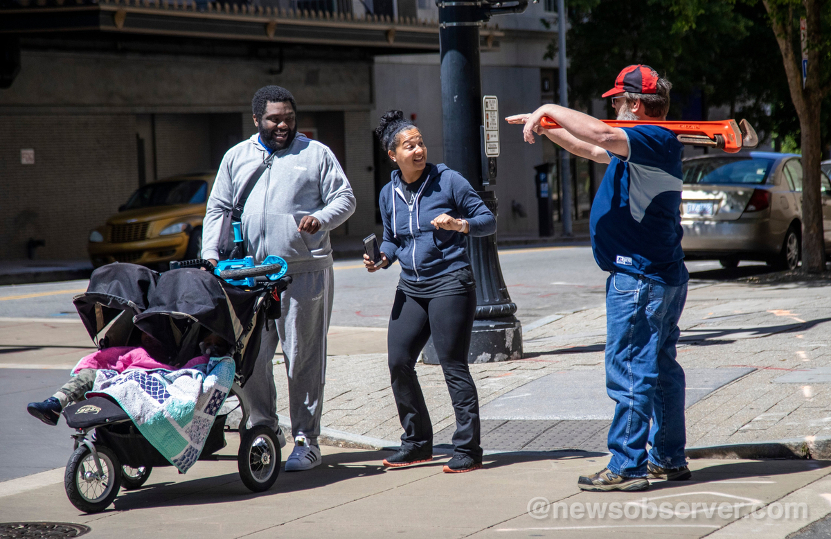 A man carrying a pipe wrench approaches a couple pushing a stroller as a group of about 11 mostly-armed demonstrators protesting the coronavirus stay-at-home order marched around downtown Raleigh and ordered sandwiches at a Subway, Saturday morning, May 9, 2020.