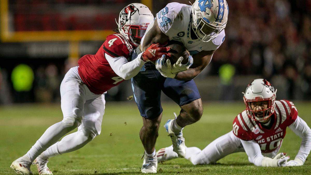 North Carolina’s British Brooks (24) breaks open for a 40-yard run in the first quarter as N.C. State’s Joshua Pierre-Louis (4) works to make the stop on Friday, November 26, 2021 at Carter-Finley Stadium in Raleigh, N.C.
