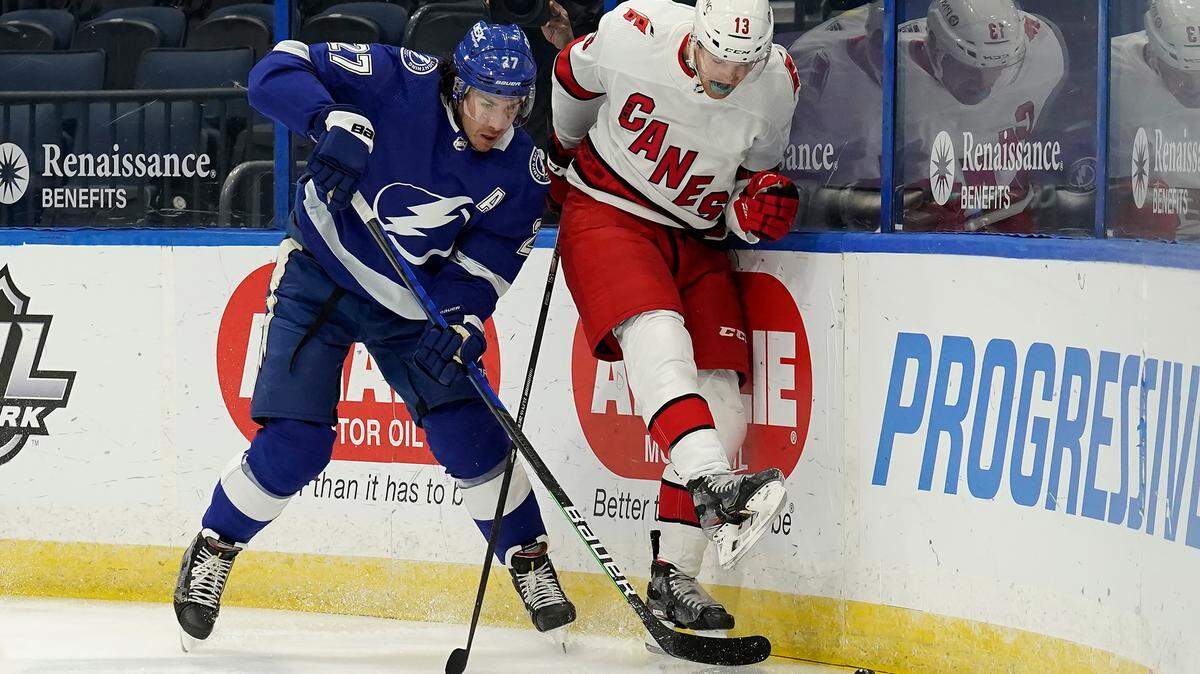 Carolina Hurricanes left wing Warren Foegele (13) kicks the puck away from Tampa Bay Lightning defenseman Ryan McDonagh (27) during the first period of an NHL hockey game Wednesday, Feb. 24, 2021, in Tampa, Fla. (AP Photo/Chris O’Meara)
