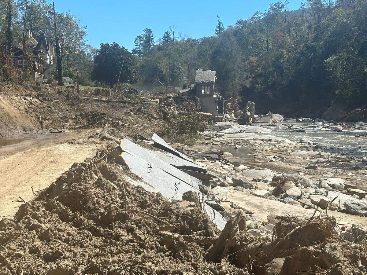 U.S. 64/74A where it passed in front of Caulder Realty & Land Co. in Bat Cave, North Carolina, as seen on Oct. 10, 2024. The pavement is still covered in several feet of mud and debris or, like most of the Caulder building, was washed away by the Rocky Broad River, right.