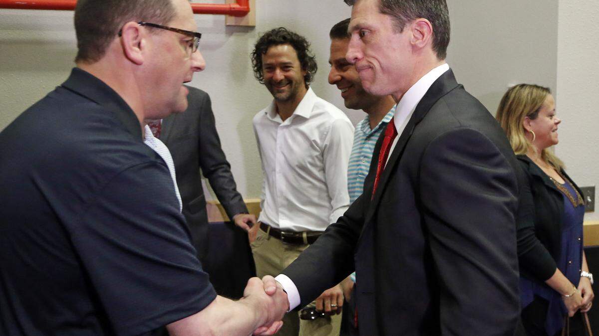 The Canes' Justin Williams, center, looks on as a well-wisher congratulates Rod Brind'Amour, right, after Brind'Amour was named the new head coach of the Carolina Hurricanes NHL team during a press conference at PNC Arena in Raleigh, NC on May 9, 2018.  Majority owner Tom Dundon also announced that Don Waddell would be the team's general manager, a position he has held in the interim since Ron Francis's departure several weeks ago.  Williams and Brind'Amour were teammates on the ice when the team won the Stanley Cup in 2006.