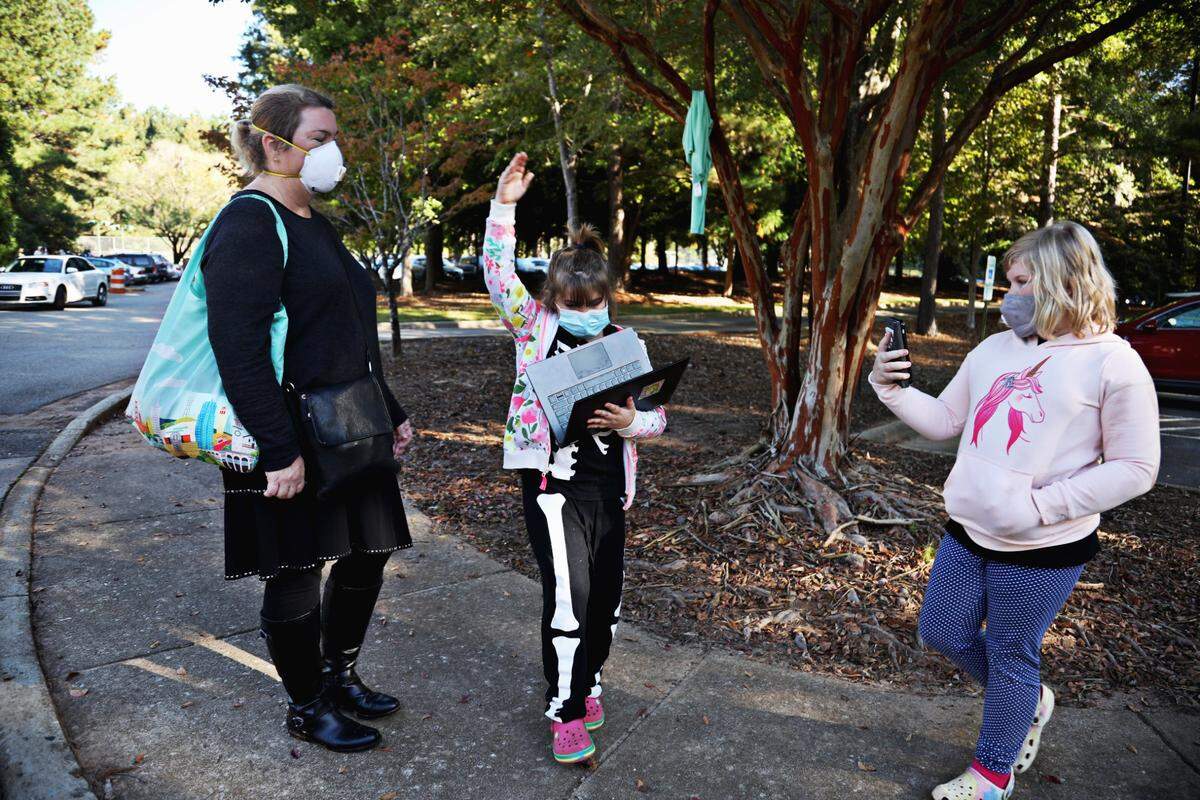 Abby Neblett, 8, center, raises her hand during an online class while her sister, Emily, 10, right, attends class via cellphone as they wait in line with their mom, Katherine, left, during early voting at Lake Lynn Community Center in Raleigh on Thursday morning, Oct. 15, 2020. Neblett says she wanted to bring her daughters to witness this moment in history so they would understand how important it is to vote.