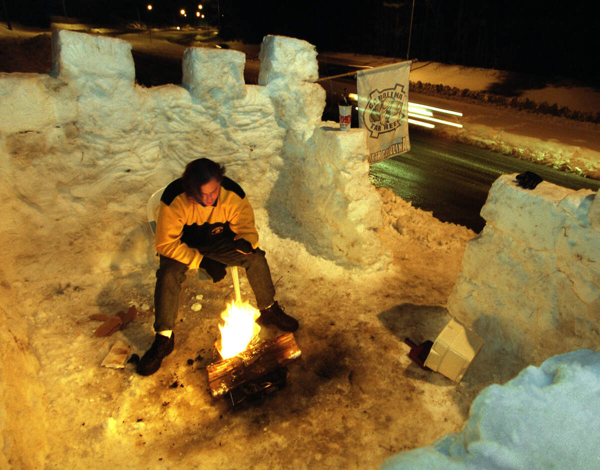 Doug Healy warms his hands by a fire Wednesday night inside the large snow fort he built beside Cary Parkway in 2000. "It just seemed like a fun thing to do." he said.