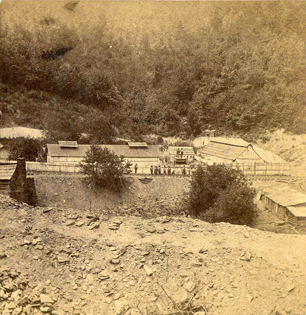Photo showing the “Stockade at Swannanoa Tunnel,” taken about 1879. About a dozen incarcerated workers stand on the tracks, with two armed guards on either side.