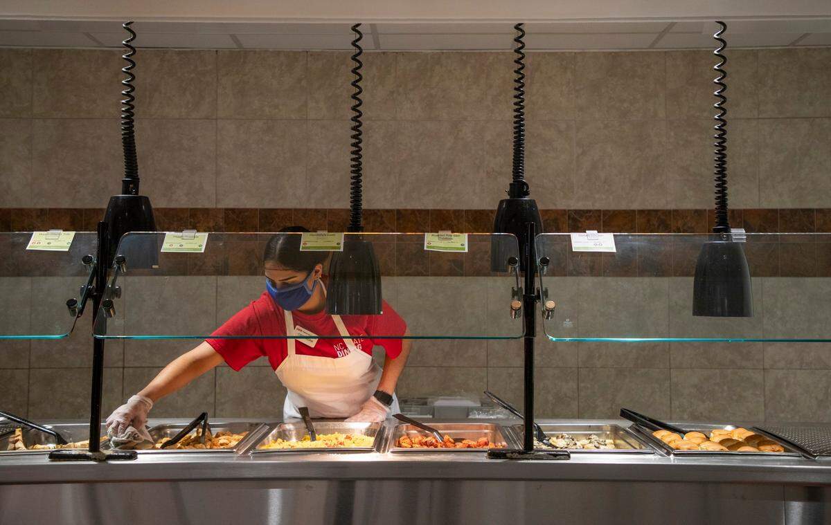 Cassandra Maya, a front line attendant, wipes her counter before serving the lunch crowd in Fountain Dining Hall at N.C. State University as it prepares for students to return to campus for the fall semester, encouraging them to follow safety protocols in place to prevent the spread of COVID-19, on Wednesday, July 22, 2020, in Raleigh, N.C.