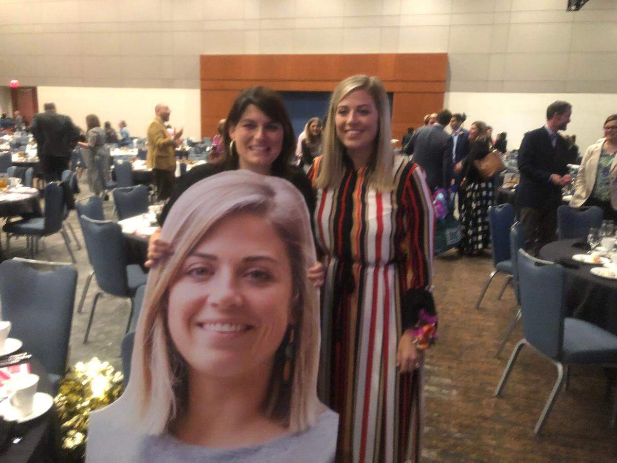 Broughton High School principal Elena Ashburn (left) poses for a photo with Caroline Olson (right) after OIson was named the 2022-23 Wake County Teacher of the Year at a May 11, 2022 ceremony at the Raleigh Convention Center. In front of them is a large-size photo of Olson provided by the school district.