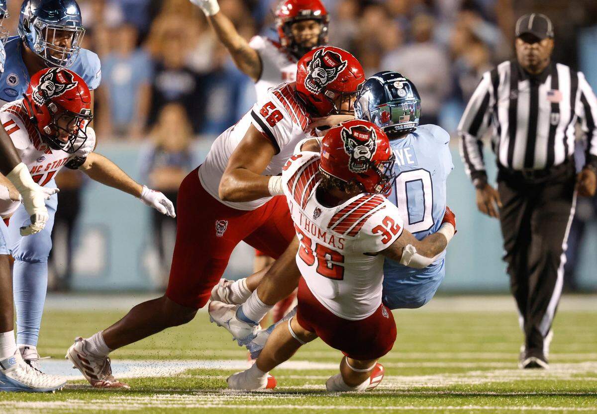 N.C. State linebacker Drake Thomas (32) and defensive end Travali Price (58) tackle North Carolina quarterback Drake Maye (10) during the second half of N.C. State’s 30-27 overtime victory over UNC at Kenan Stadium in Chapel Hill, N.C., Friday, Nov. 25, 2022.