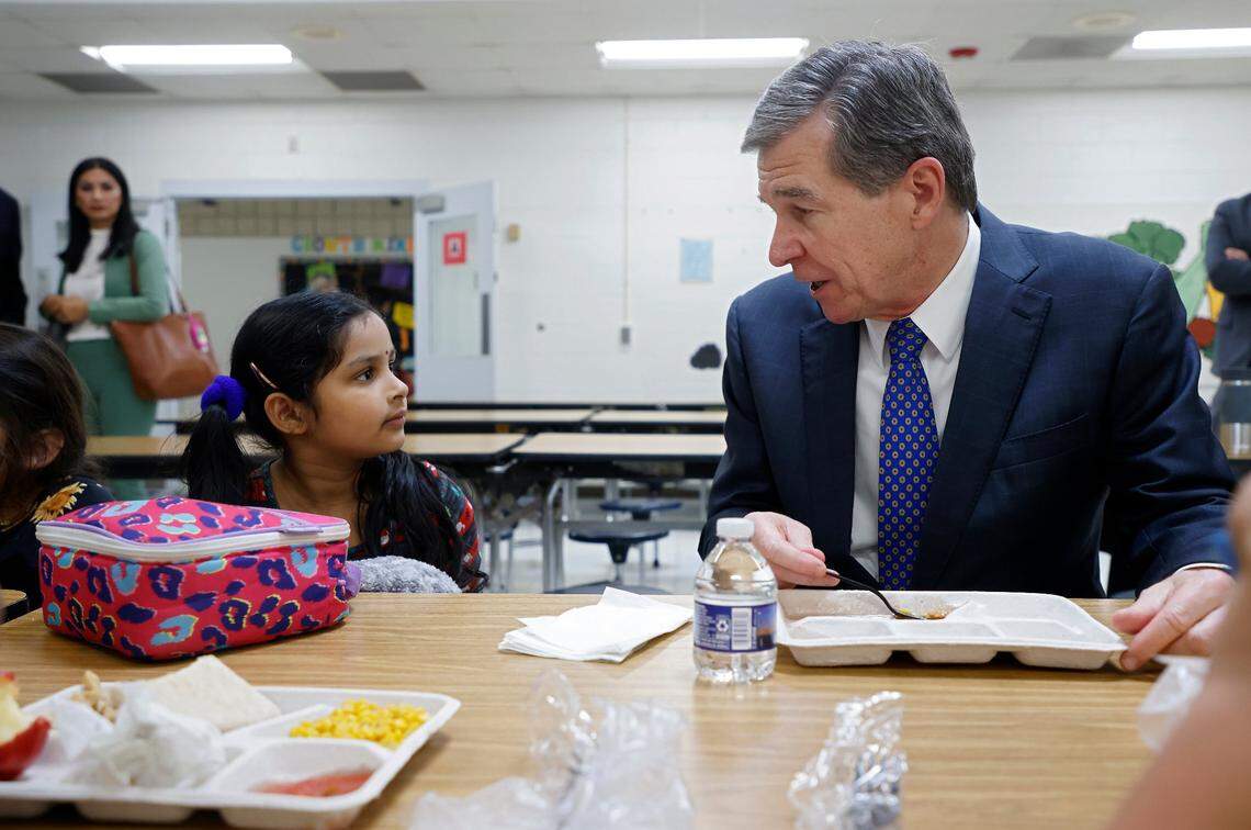 Gov. Roy Cooper speaks with kindergarten student Sankeerthana Lolla while eating lunch at Bethesda Elementary School in Durham, N.C in October 2022. Cooper visited the school to announce new agreements to bring food from North Carolina farmers and producers to schools.