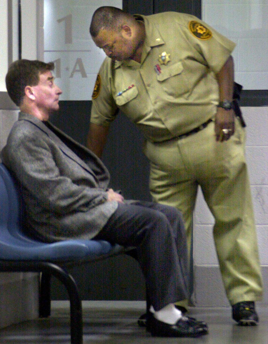 Michael Peterson sits as Durham County Detention officer Darryl Lunsford looks through his personal belongings as he is processed in the Magistrate’s office, Dec. 20, 200,1 after being indicted in connection with the death of his wife.