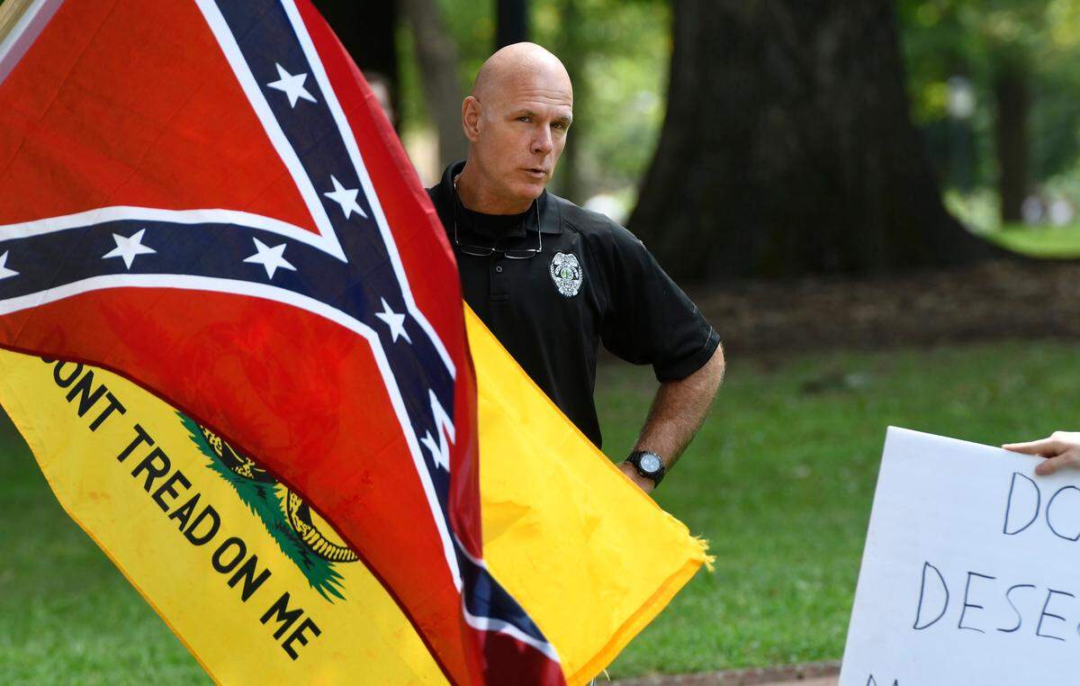 UNC police chief Jeff McCracken talks with five men carrying Confederate flags standing near a sit-in at the base of the Silent Sam Confederate statue on the UNC campus Saturday, Aug. 26, 2017. The small group, who refused to give their names, was standing in opposition to a larger group of protesters calling for the removal of the statue.