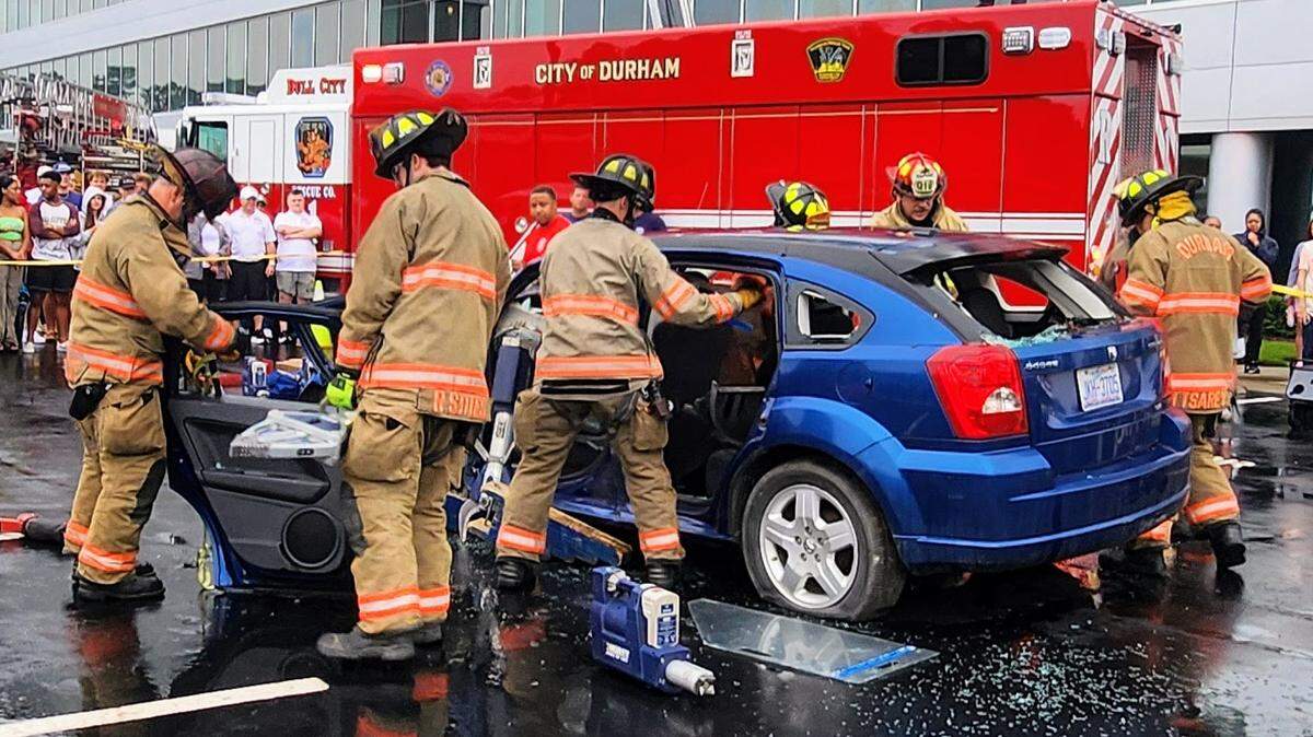 Firefighters taking apart a blue car in front of a red truck.