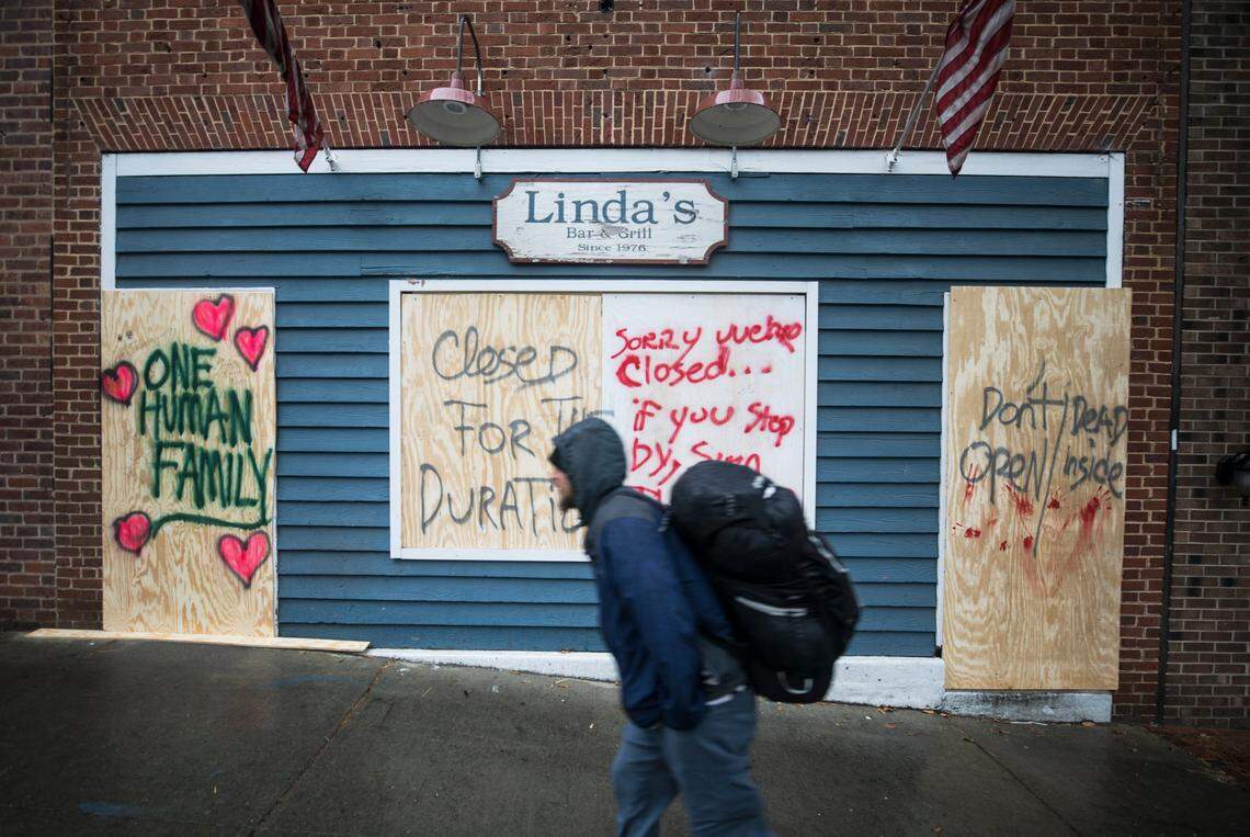A man walks down Franklin St. in Chapel Hill, NC past a boarded up Linda’s Bar and Grill on Monday, March 23, 2020. The restaurant and bar closed on Saturday for the duration of the coronavirus public health crisis. The business is encouraging people to leave messages on the boards and to donate to a GoFundMe campaign set up for their staff.