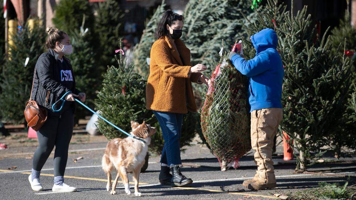 Katie Lust, her dog Cruiser, and Taylor Young purchase a Christmas tree at the State Farmers Market on Tuesday, December 8, 2020 in Raleigh, N.C. Half of the tree vendors have sold out at the market in the first week of December.