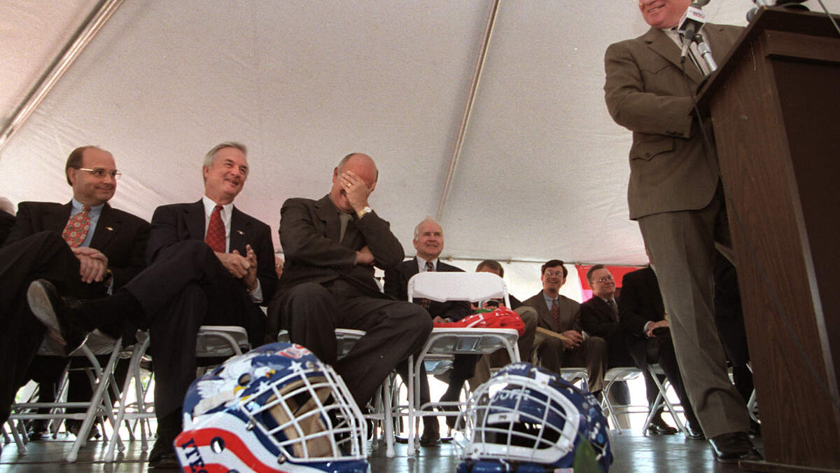 Hartford Whalers owner Peter Karmanos (center) reacts to a joke by Steve Stroud (podium) about a Stanley Cup playoff game being held soon in the new arena during 1997 ceremonies announcing that the Whalers will move to Raleigh. From left: Speaker of the N.C. House of Representatives Harold Brubaker, Governor Jim Hunt, Karmanos, and Stroud.