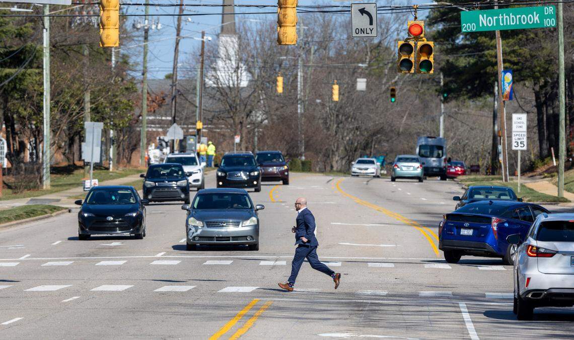 A pedestrian crosses Six Forks Road at the intersection of Northbrook Drive on Wednesday, February 21, 2024 in Raleigh, N.C. The road is being widened thanks in part to a $14 million federal grant.