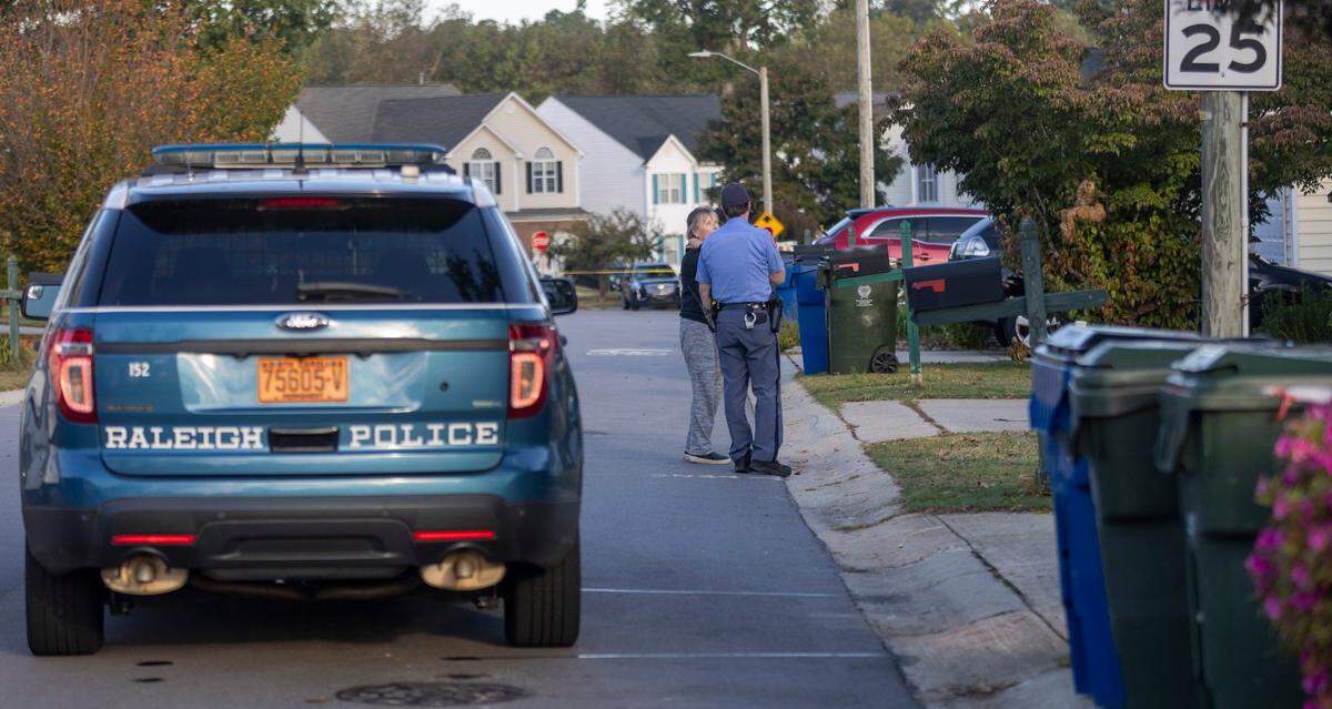 Raleigh Police talk with a resident on Castle Pines Drive in the Hedingham neighborhood on Friday morning, October 14, 2022 in Raleigh, N.C. as they continue to investigate the killing of five people yesterday on the greenway nearby.