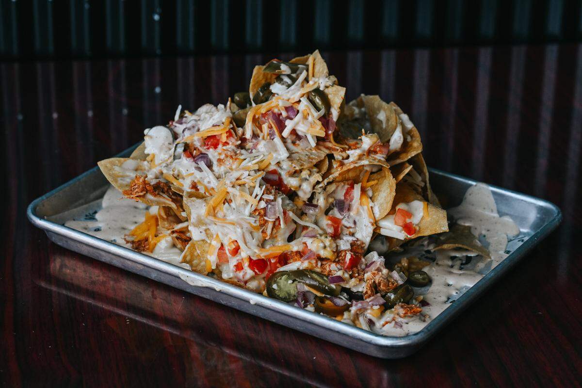 Chicken tinga trash can nachos are topped with Mexican street corn queso, chipotle chicken tinga, shredded cheddar jack cheese, tomatoes, red onions and jalapenos, drizzled with poblano queso.