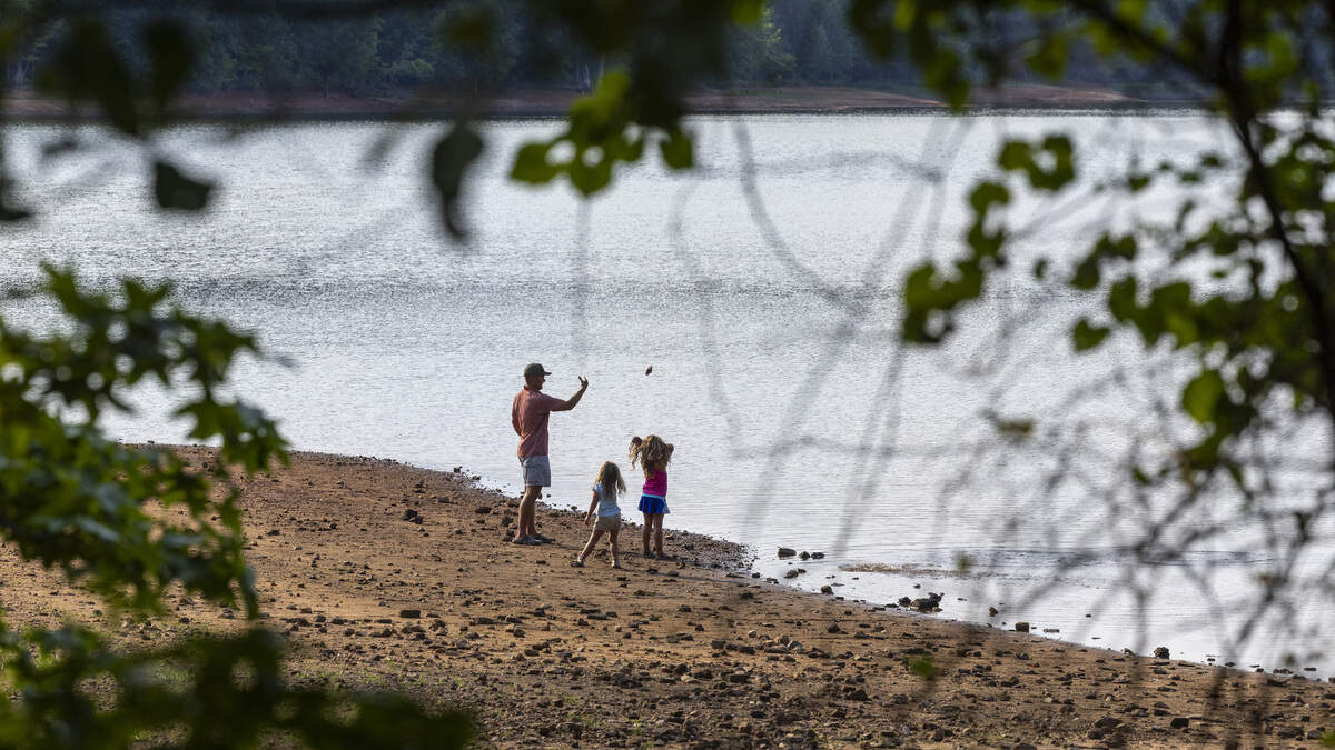 Scott Beasley and his daughters, Virginia Beasley, 3, center, and Ada Beasley, 5, right, toss rocks into Falls Lake from the receded shoreline at Forest Ridge Park in Raleigh on Thursday, June 25, 2026. Raleigh is 18.59 inches below its average rainfall since August 2025, and Falls Lake, Raleigh's primary water source, is 5 feet below its target level. As of mid-June, Durham was about 10 to 12 inches below normal rainfall since the start of the year.
