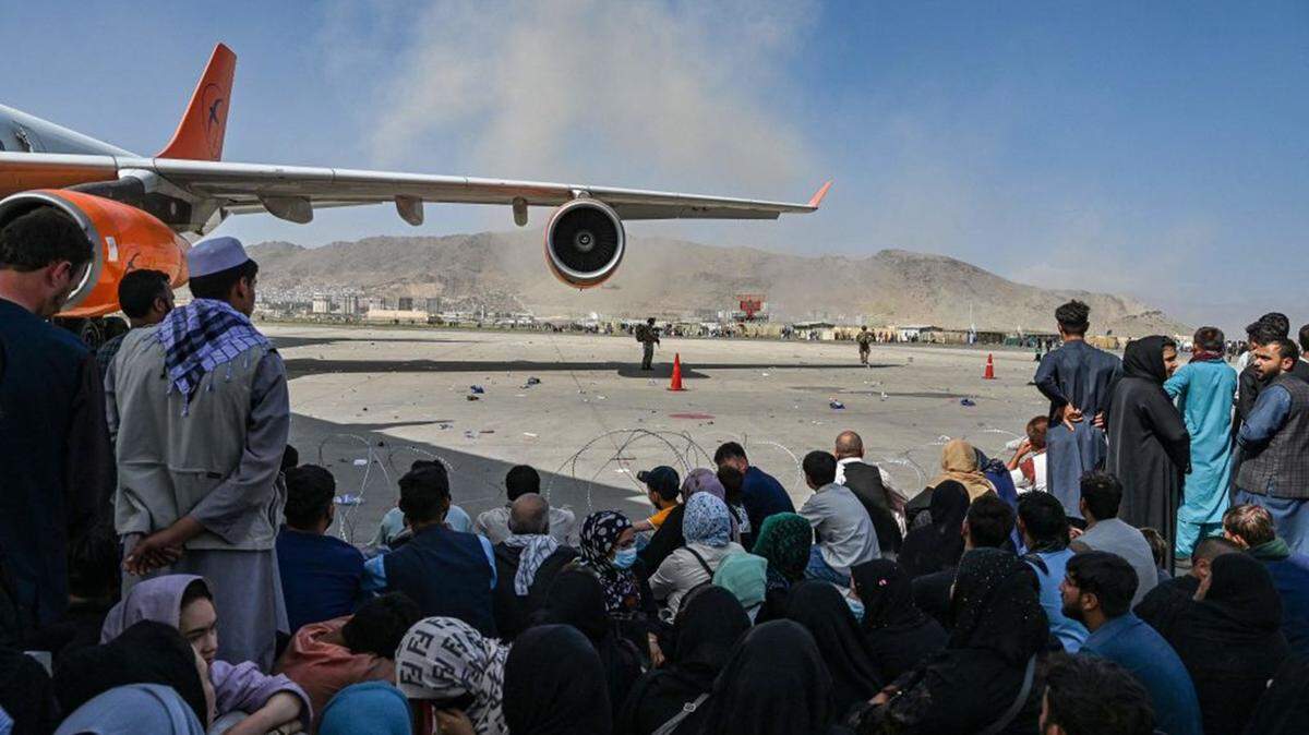 Afghan people sit as they wait to leave the Kabul airport in August 2021. After a stunningly swift end to Afghanistan’s 20-year war and the withdrawal of the US military, thousands of people mobbed the airport trying to flee Taliban rule.