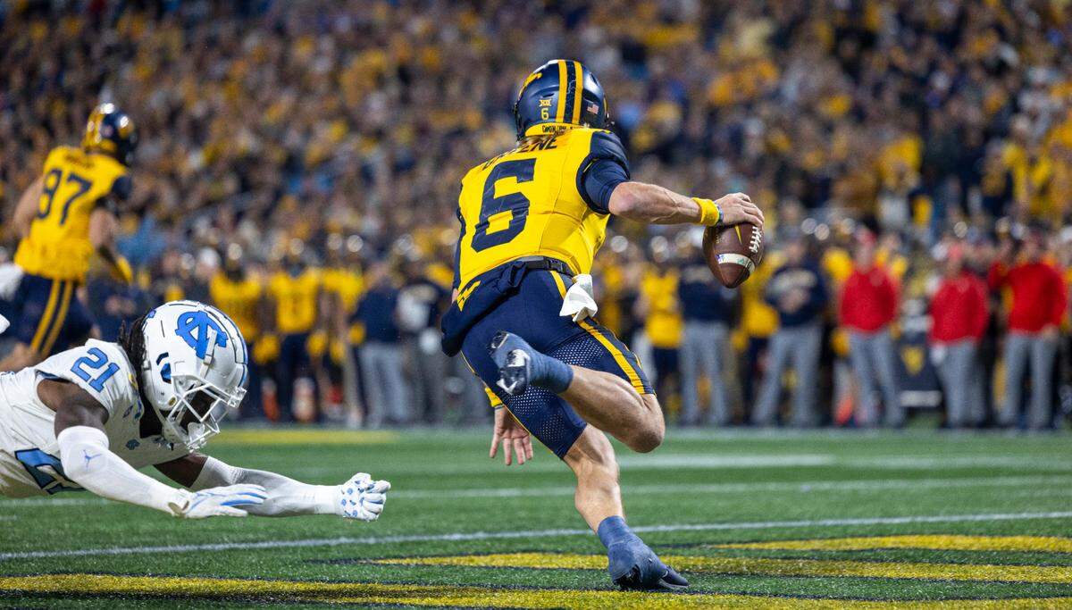 West Virginia quarterback Garrett Greene (6) escapes the grasp of North Carolina’s Kaleb Cost (21) as he sprints out of the end zone in the first quarter during the Duke’s Mayo Bowl on Wednesday, December 27, 2023 at Bank of American Stadium in Charlotte, N.C.