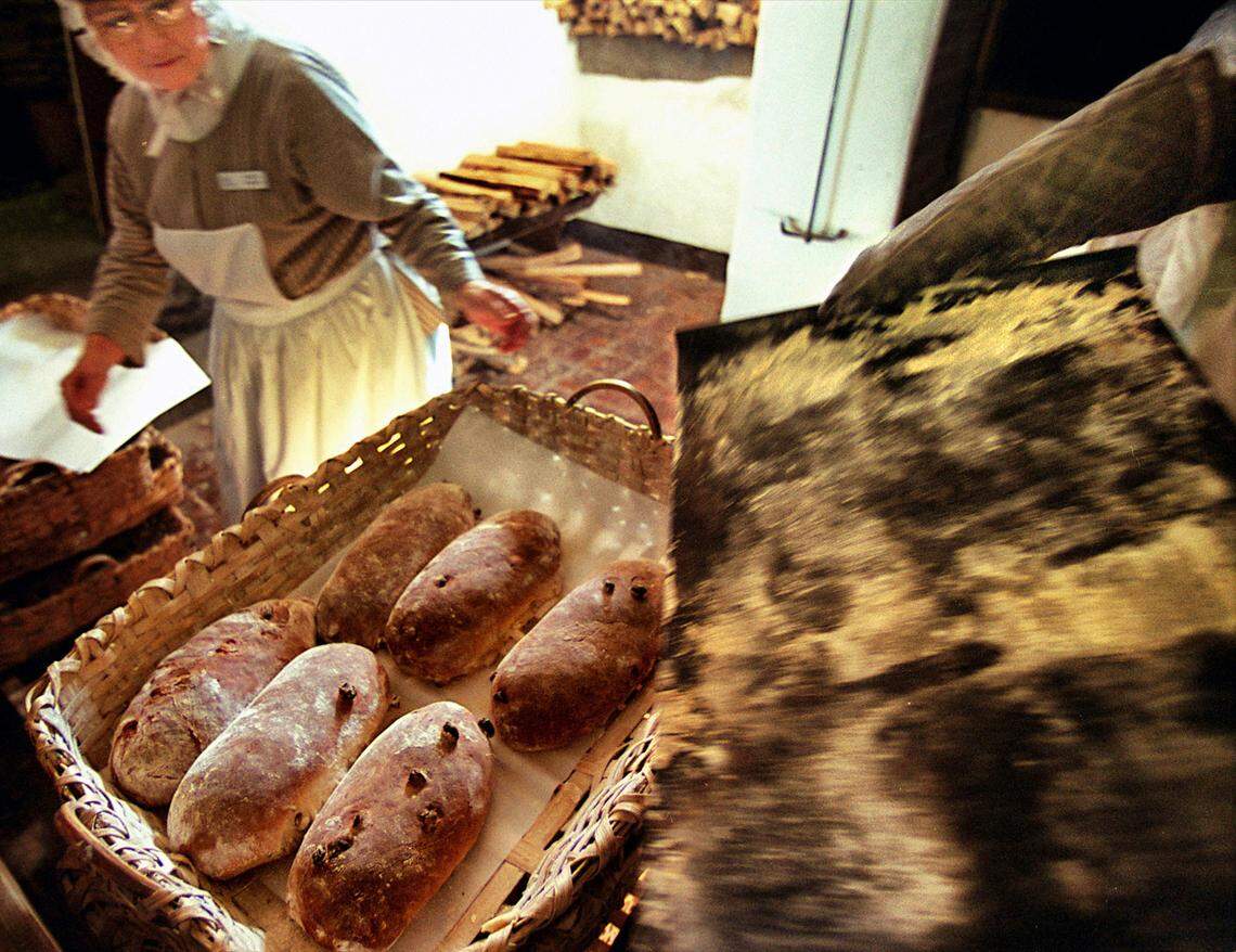 Loaves of hot raisin bread just out of the oven slide off of a pan and into a handmade basket in the Winkler Bakery at Old Salem.