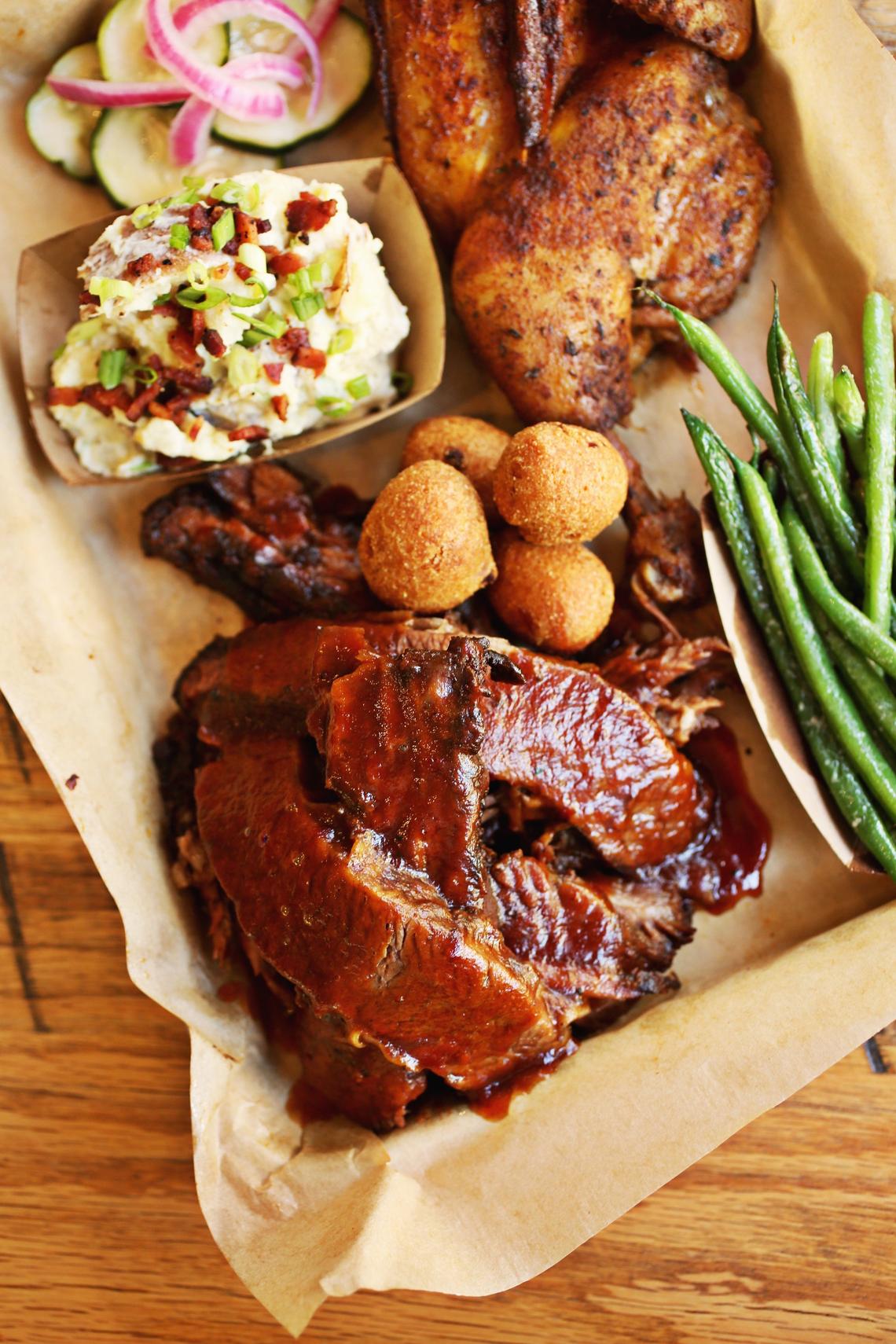 Southern Charred’s smoked half chicken, top right, and Texas-style beef brisket, bottom left, is served here with garlic herb green beans, sweet onion hush puppies, southern potato salad topped with bacon and homemade pickles.
