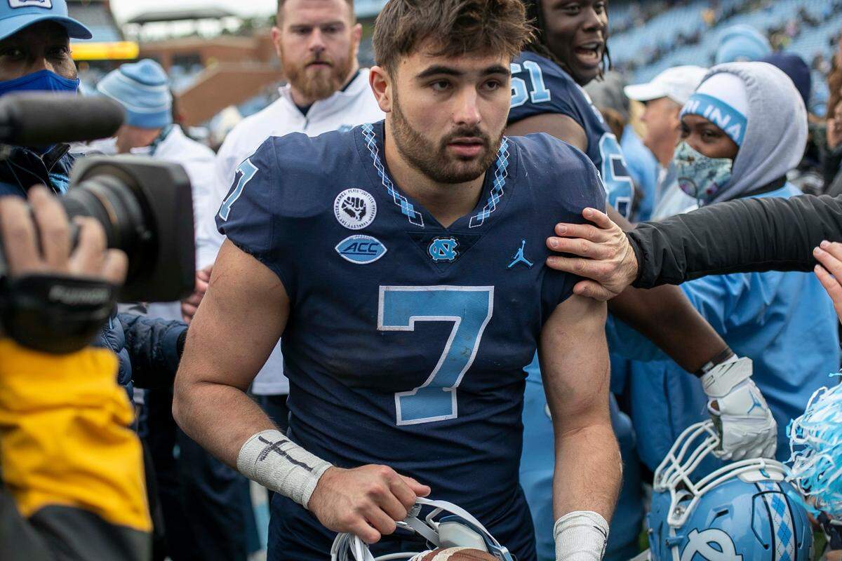 North Carolina quarterback Sam Howell (7), carrying a game ball in his helmet, works his way through fans that stormed the field, following the Tar Heels’ 58-55 victory over Wake Forest on Saturday, November 6, 2021 at Kenan Stadium in Chapel Hill, N.C.