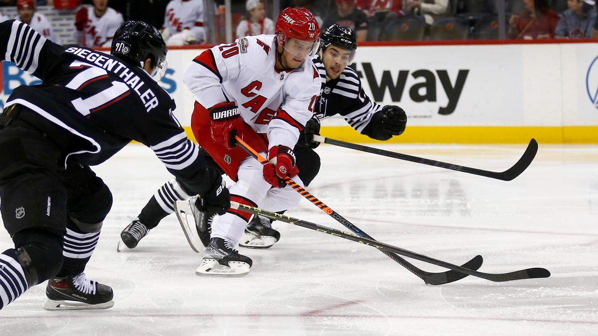 Carolina Hurricanes center Sebastian Aho (20) skates between New Jersey Devils defenseman Jonas Siegenthaler, left, and center Nico Hischier during the second period of an NHL hockey game, Sunday, Jan. 1, 2023, in Newark, N.J. (AP Photo/John Munson)