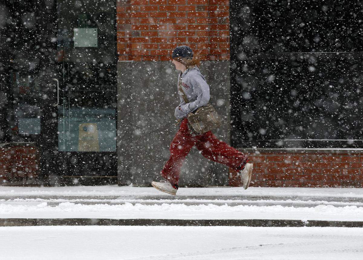A person runs along Corcoran Street as snow falls in Durham, N.C. on Wednesday, Feb. 19, 2025.