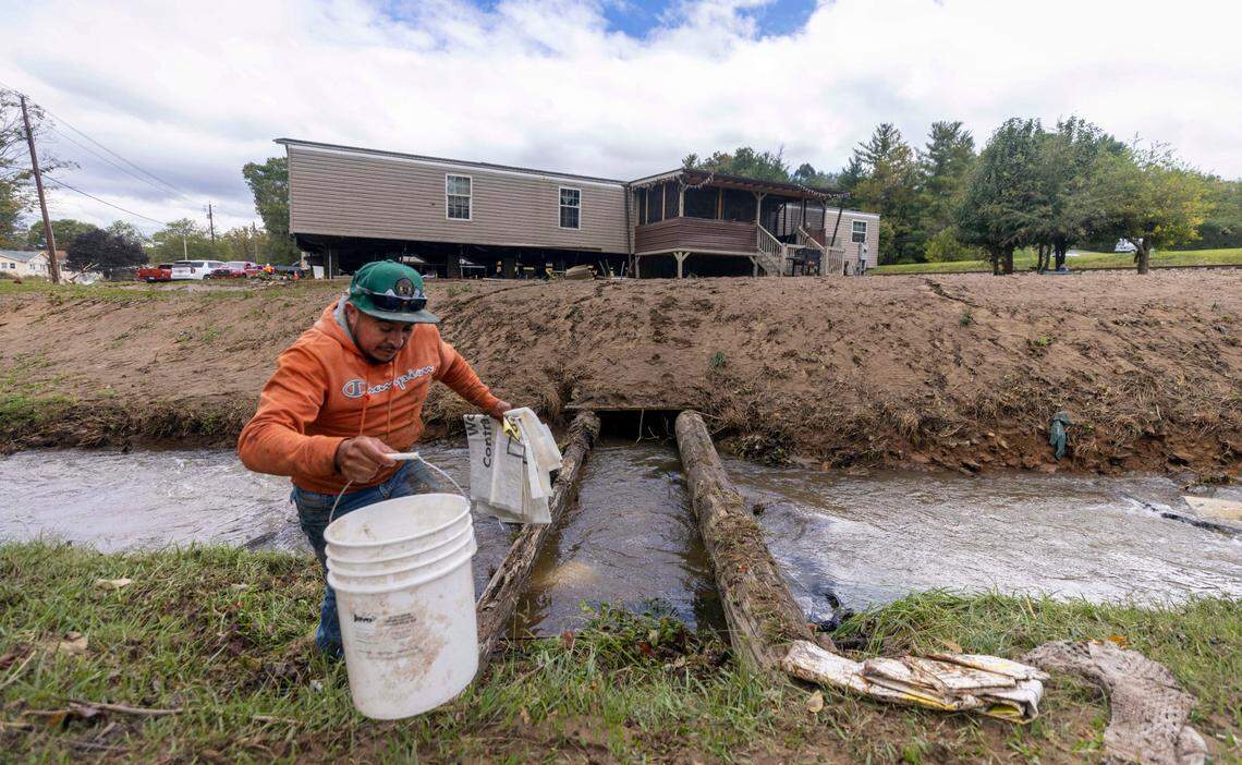 Estaban Sanchez retrieves water from a creek to be used for cleaning a flooded home in Clyde on Saturday, Sept. 28, 2024 after massive flooding damaged dozens of homes and businesses. The remnants of Hurricane Helene caused widespread flooding, downed trees, and power outages in western North Carolina.